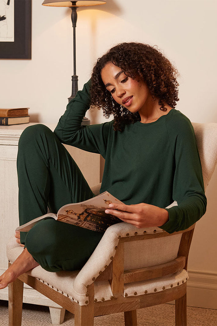 Cyberjammies 5656 Ember Dark Green Slouch Jersey Long Sleeve Pyjama Top, worn sitting in a chair