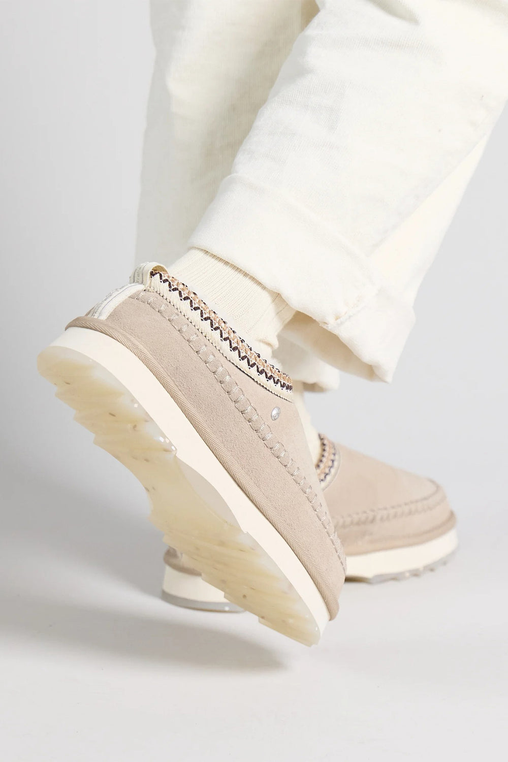 Beige casual shoe worn with white pants on a light gray background