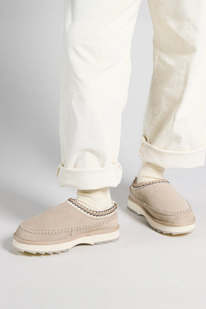 Beige shoes worn with light-colored pants on a plain background