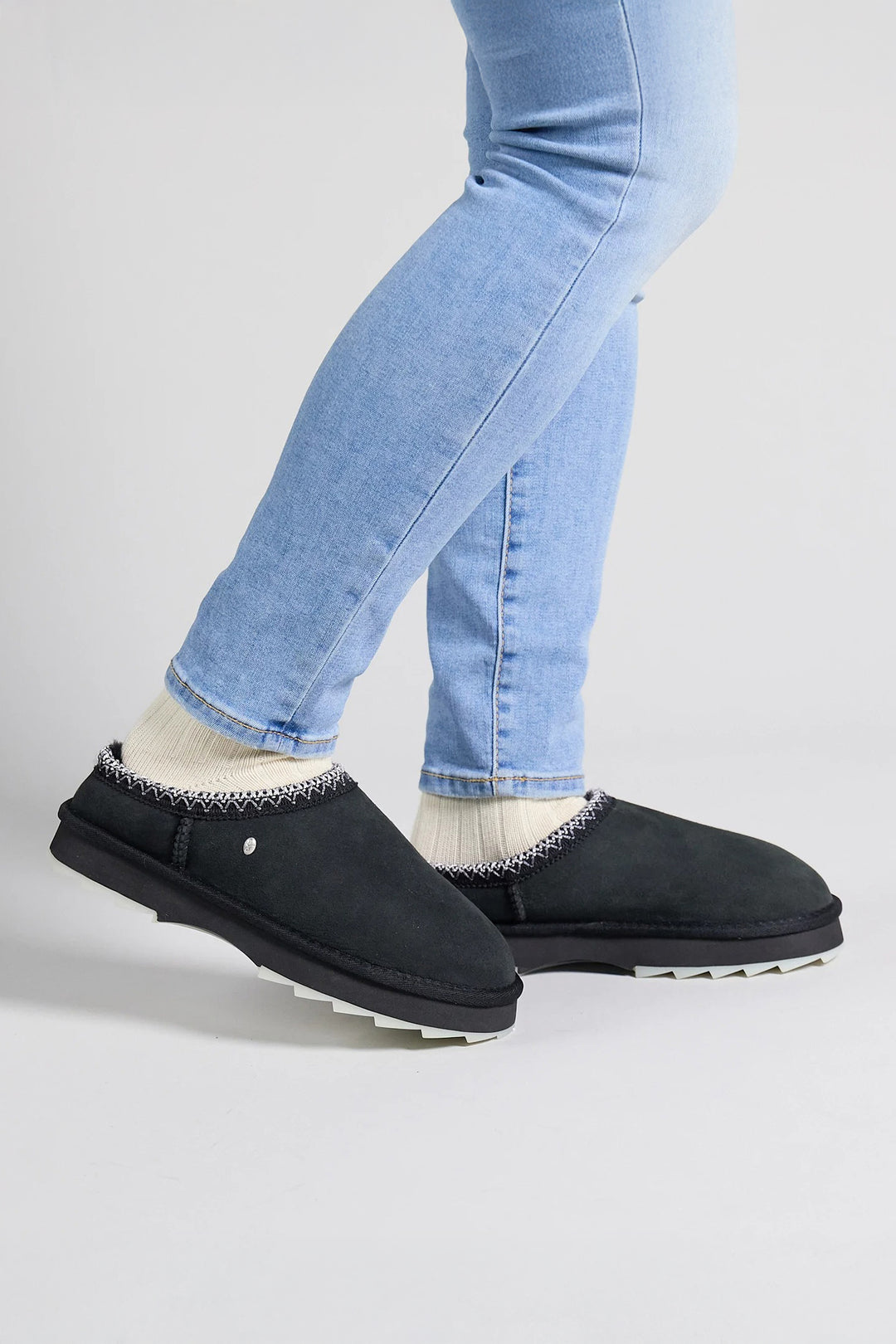 Black slip-on shoes worn with light blue jeans on a white background