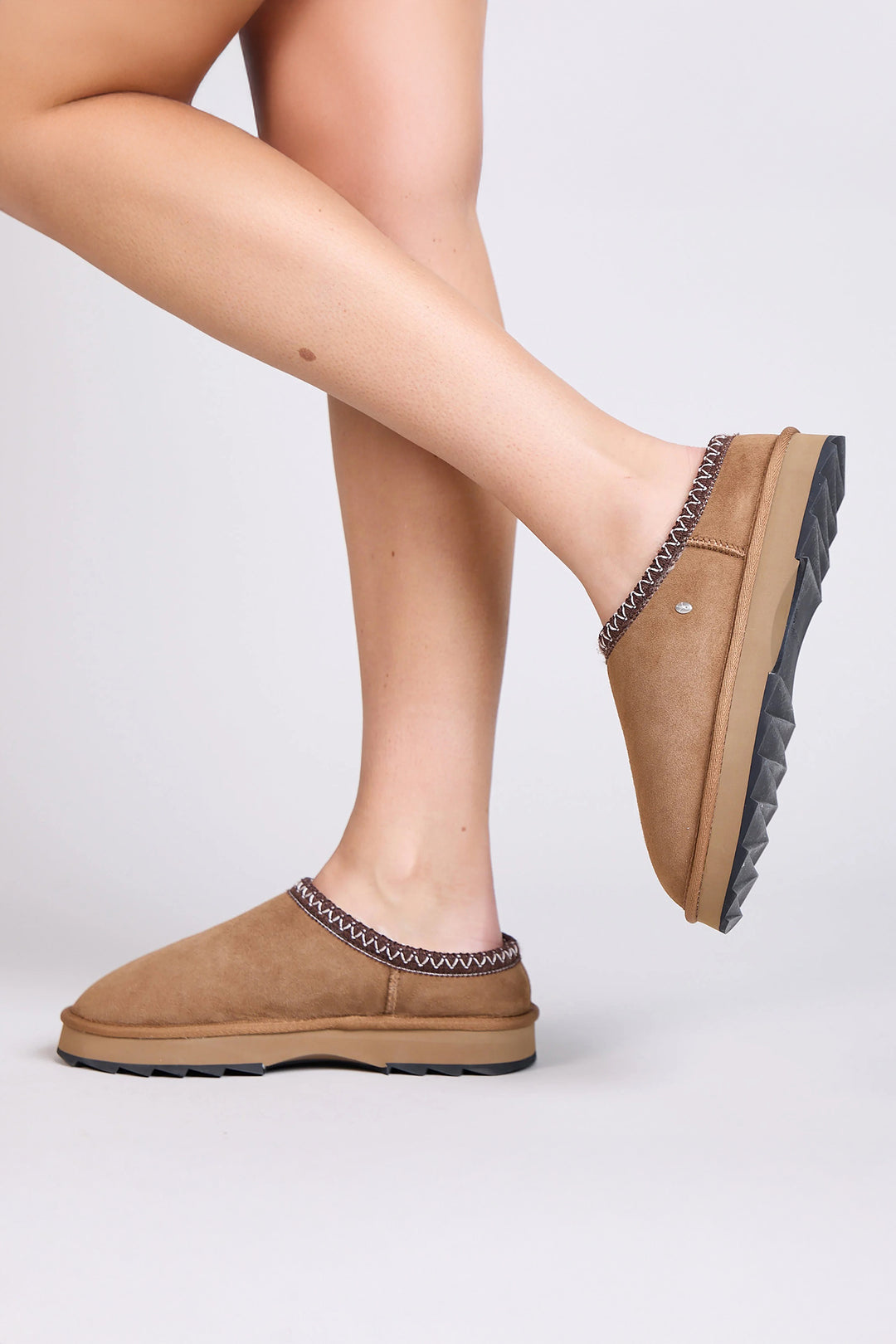 Tan slippers worn by a person on a light gray background