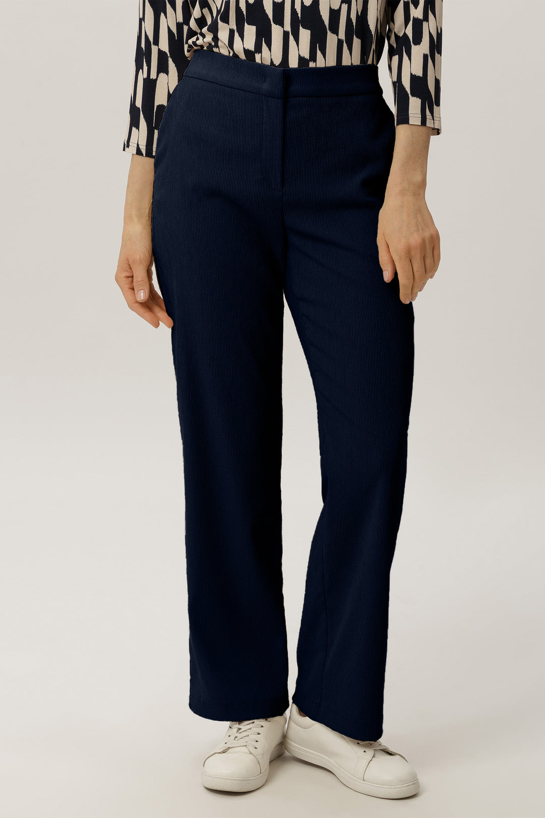 Person wearing navy pants and a patterned shirt on a white background