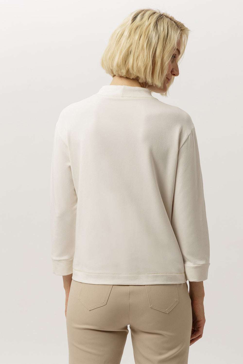 Woman wearing a beige sweater and pants against a white background