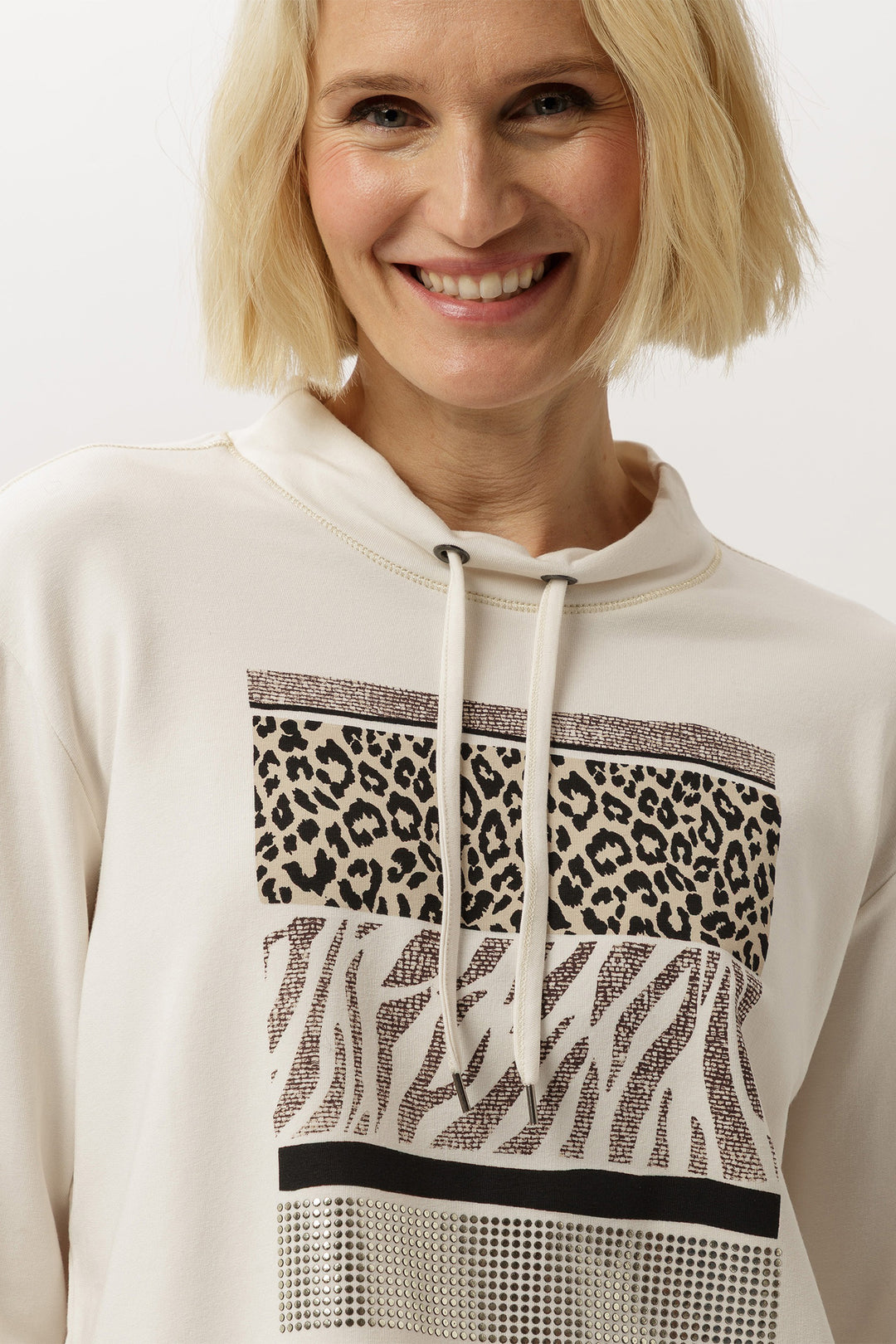 Woman wearing a white hoodie with animal print patterns on a plain background
