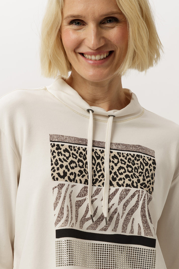 Woman wearing a white hoodie with animal print patterns on a plain background