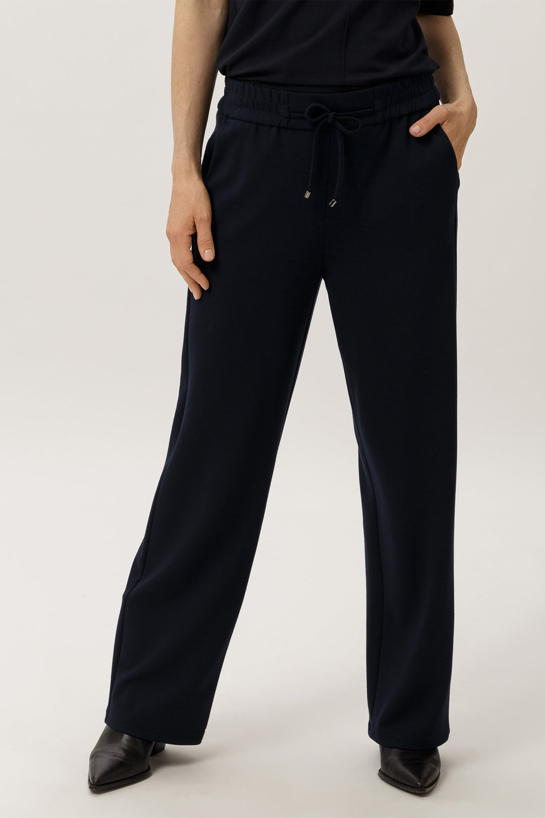Person wearing navy pants and a black top on a white background