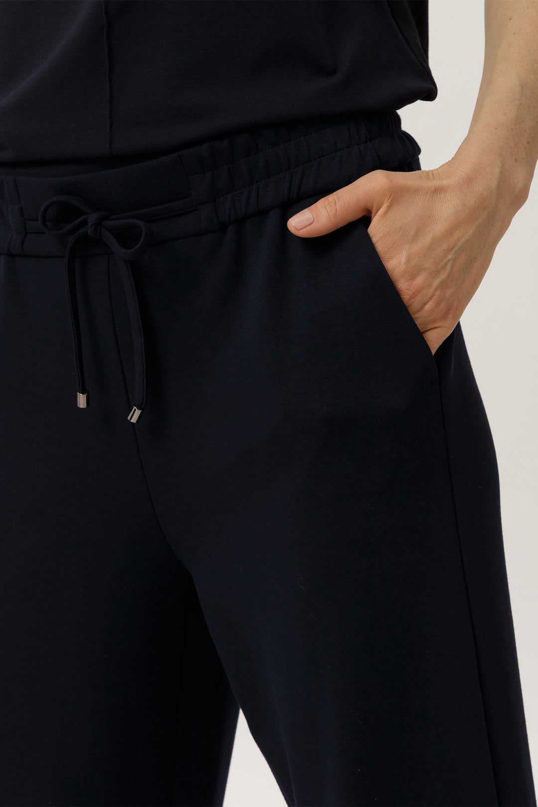 Person wearing navy pants with a drawstring waist on a plain background
