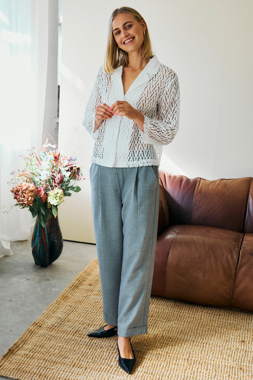 Woman in a light blue knitted cardigan and gray pants standing in a living room.