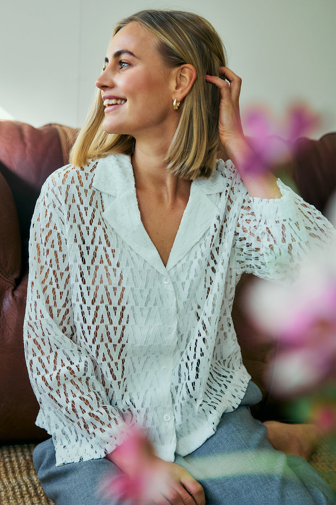 Woman wearing a white lace top sitting on a couch with blurred flowers in the foreground