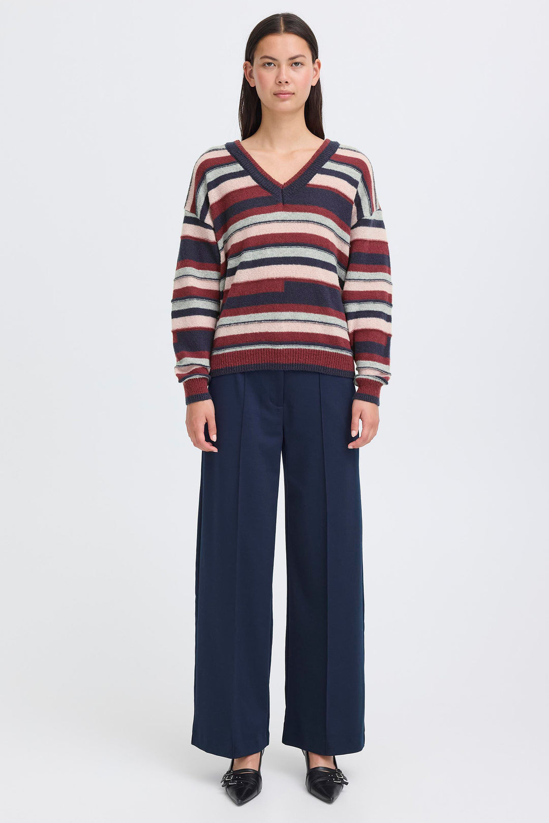 Woman wearing a striped sweater and navy pants on a white background