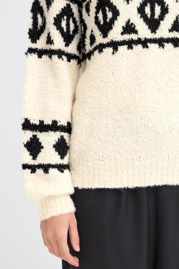 Close-up of a cream sweater with black geometric patterns on a plain background