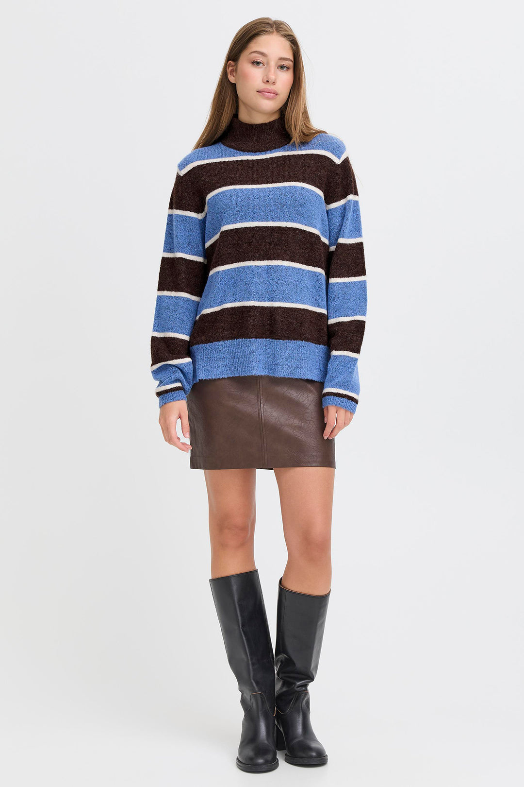 Woman wearing a striped sweater and leather skirt with black boots on a white background