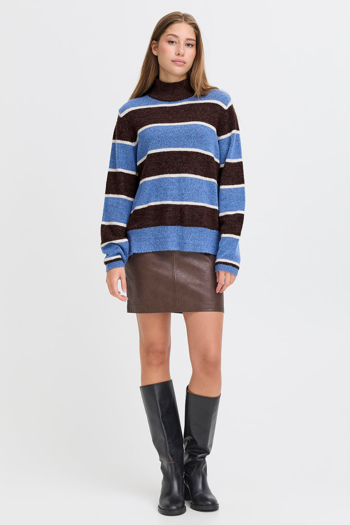 Woman wearing a striped sweater and leather skirt with black boots on a white background