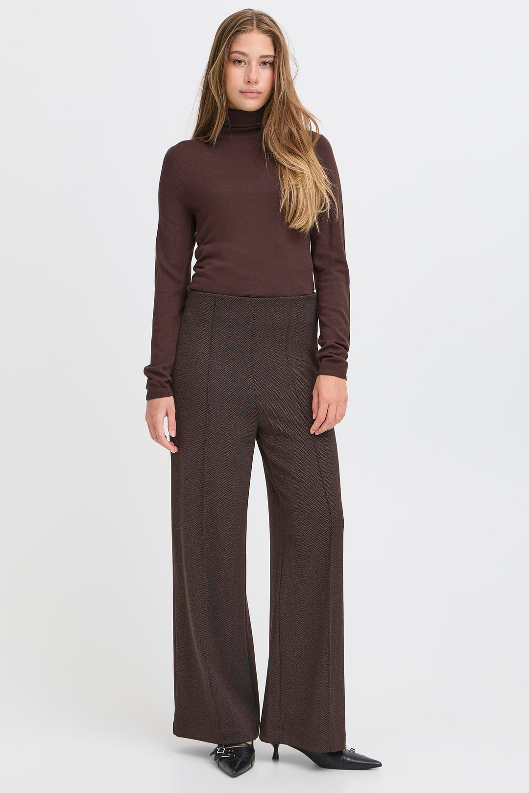 Woman wearing a brown turtleneck and wide-leg pants on a white background