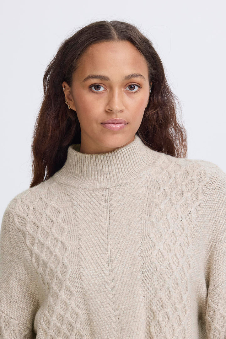 Woman wearing a beige cable knit sweater against a plain background