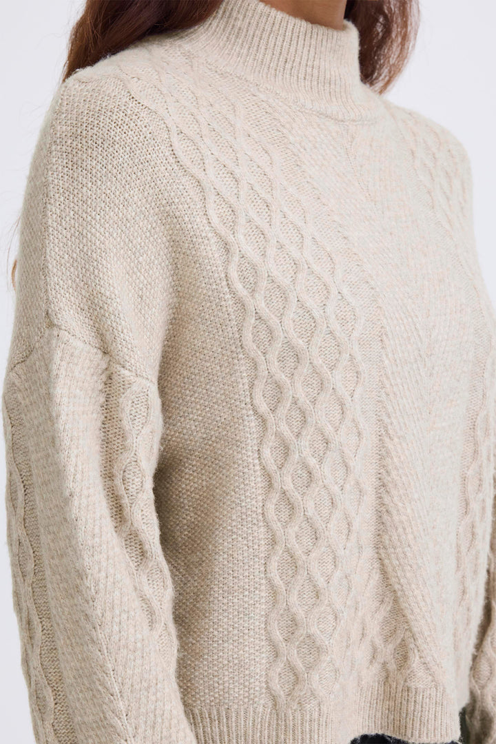 Beige cable knit sweater worn by a person on a white background