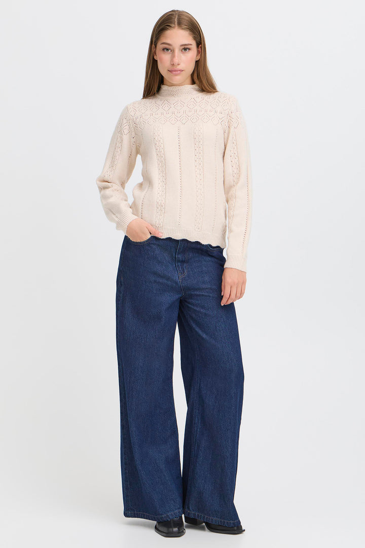 Person wearing a cream sweater and blue jeans on a white background