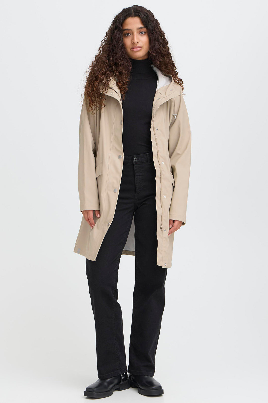 Person wearing a beige trench coat over a black outfit on a white background