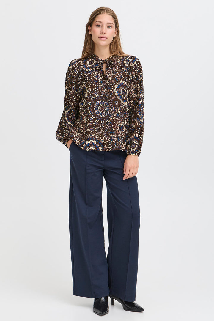 Woman wearing a patterned blouse and navy pants on a white background