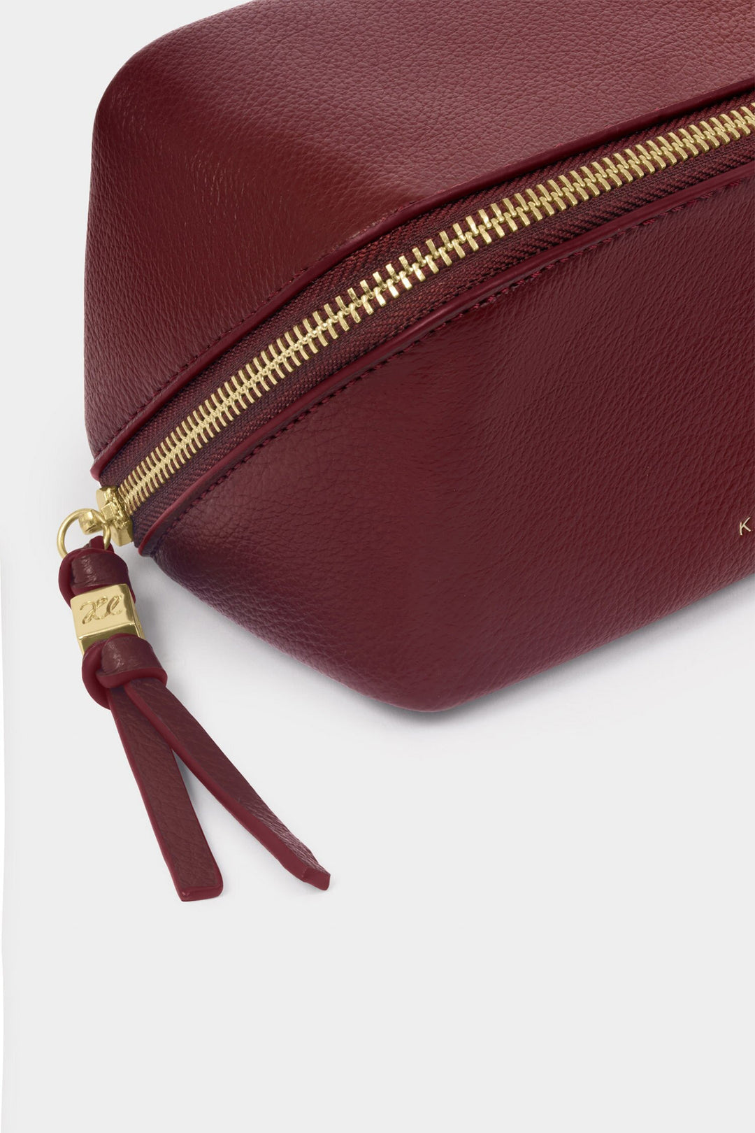 Maroon pouch with gold zipper and tassel on a light gray background