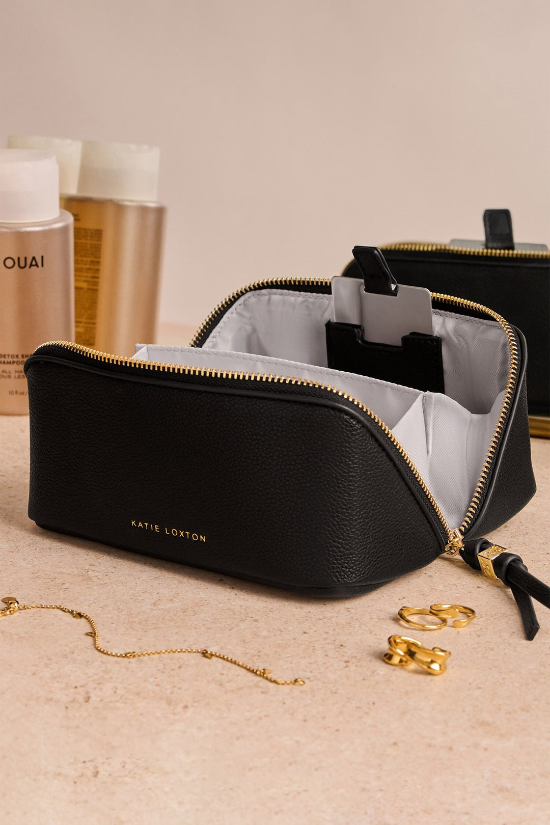 Black cosmetic bag with gold interior, gold jewelry, and bottles in the background