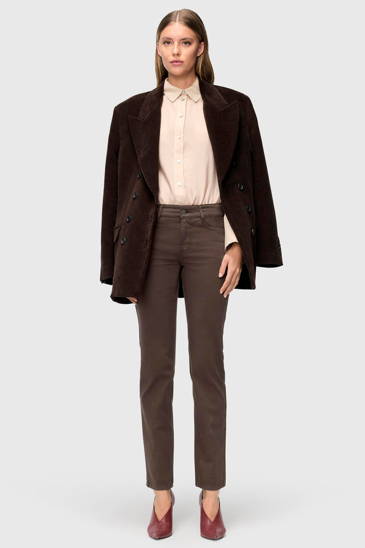 Woman wearing a brown coat, beige shirt, and brown pants on a white background