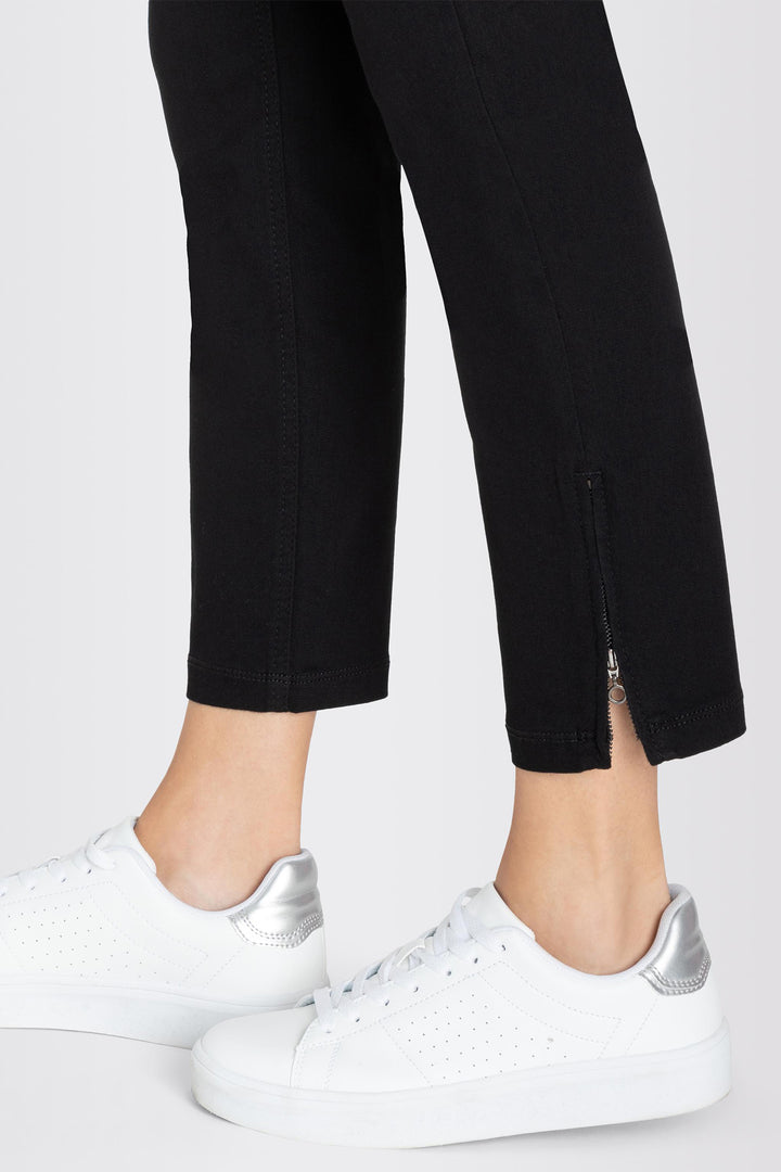 Person wearing black pants with a zipper and white sneakers on a light gray background
