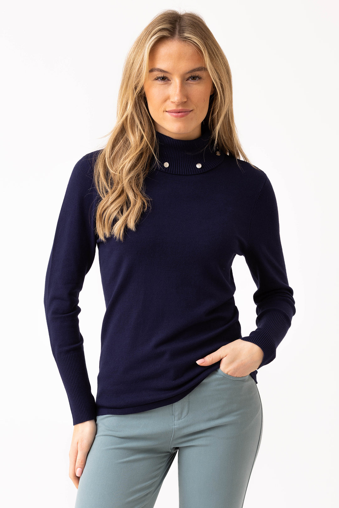 Woman wearing a navy blue turtleneck sweater and light gray pants on a white background
