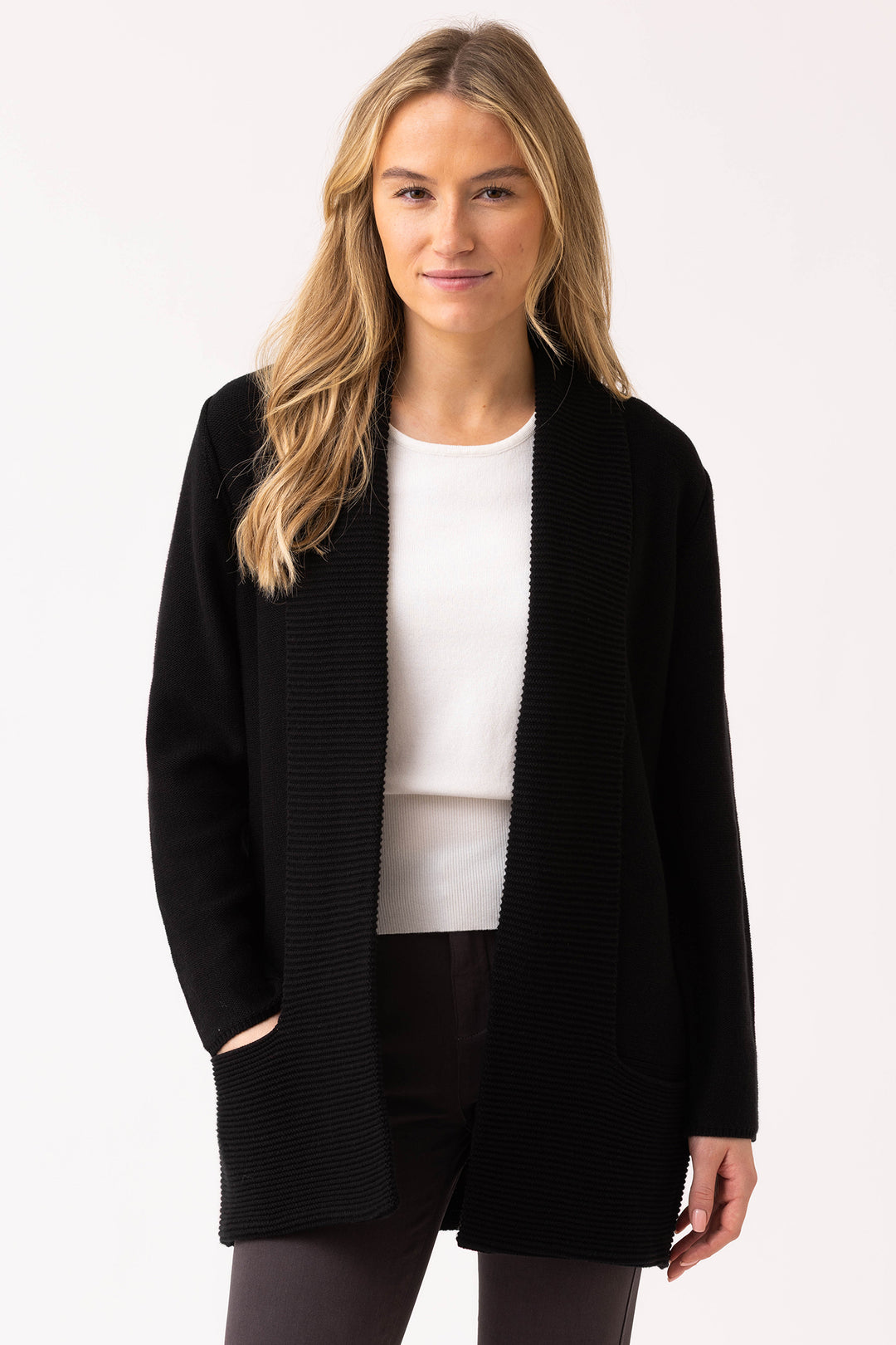 Woman wearing a black cardigan over a white shirt and black pants on a white background