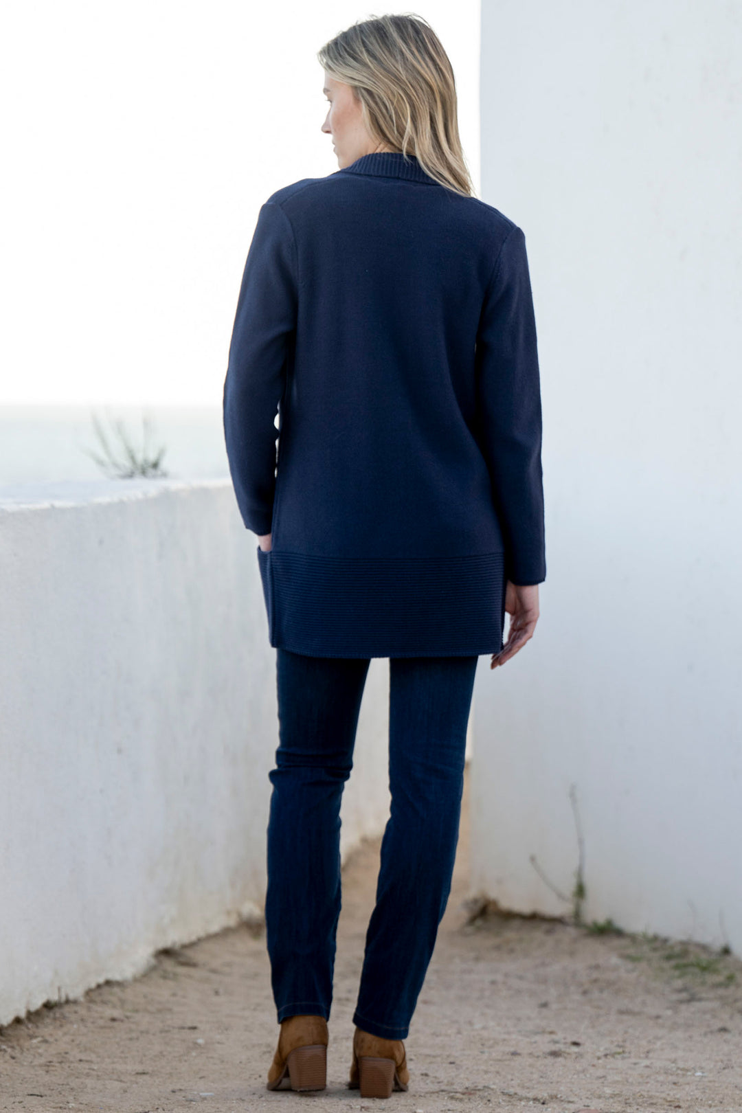 Person wearing a navy blue coat and pants standing against a white wall.