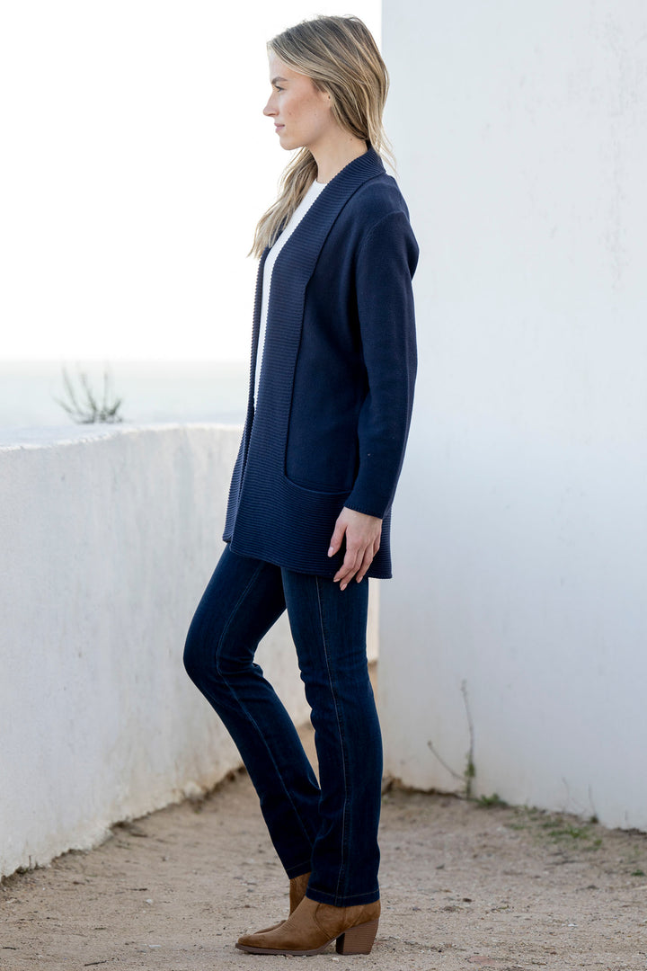 Woman wearing a navy cardigan standing against a white wall.