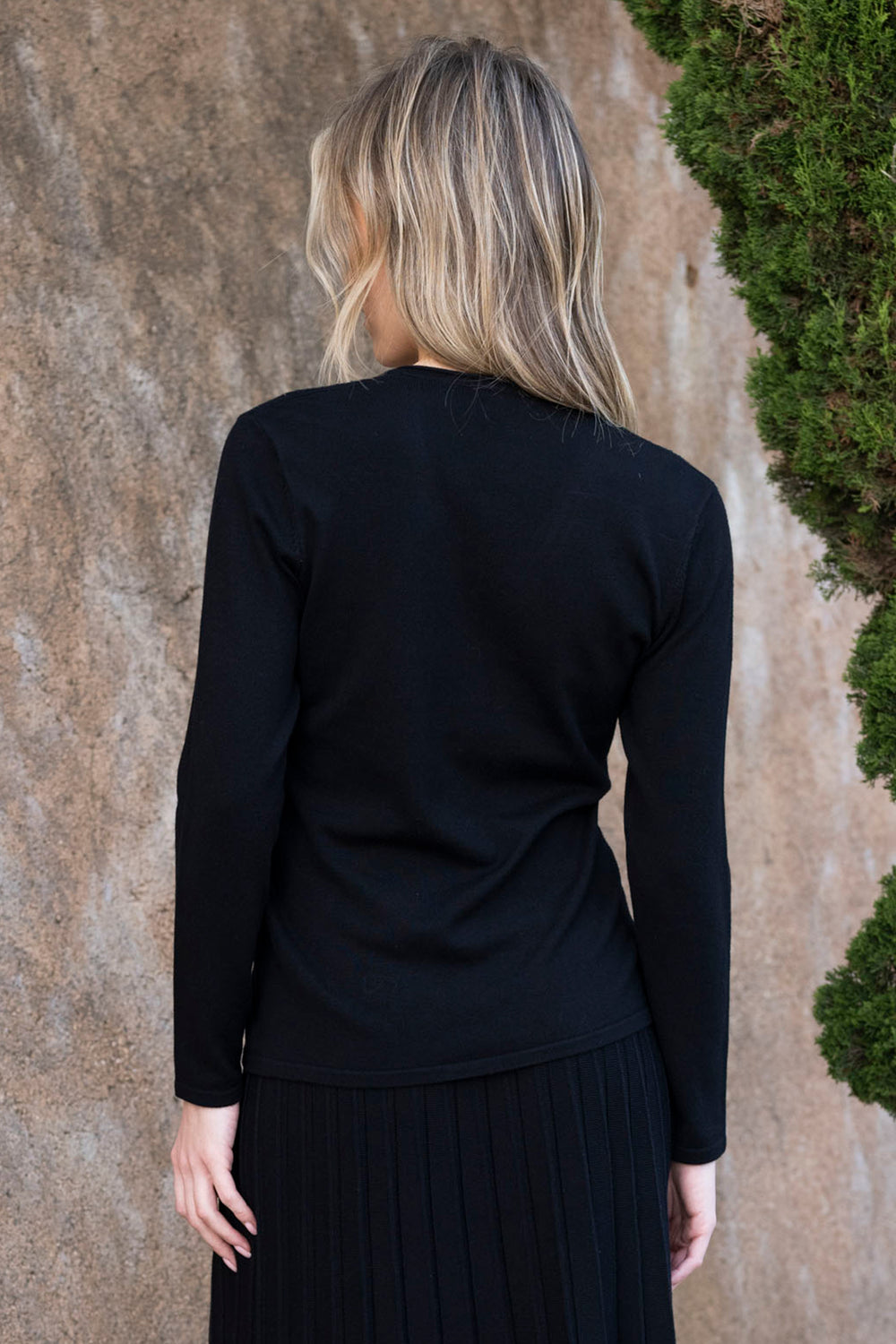 Person wearing a black long-sleeve top and dark pants against a textured wall.