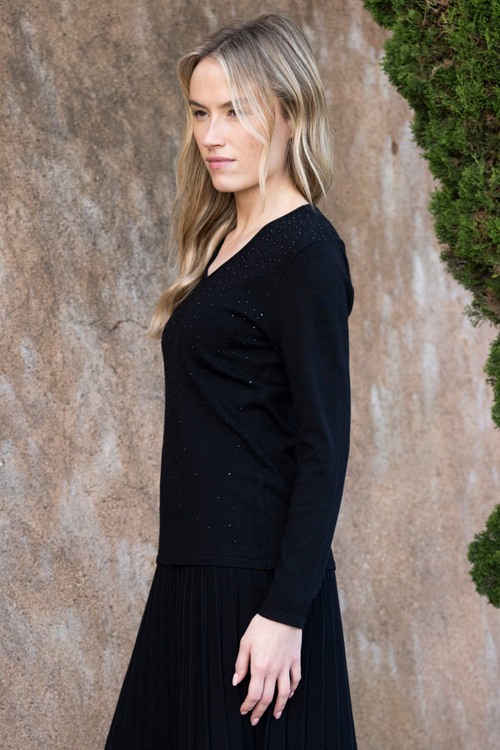 Woman wearing a black long-sleeve top against a textured wall.