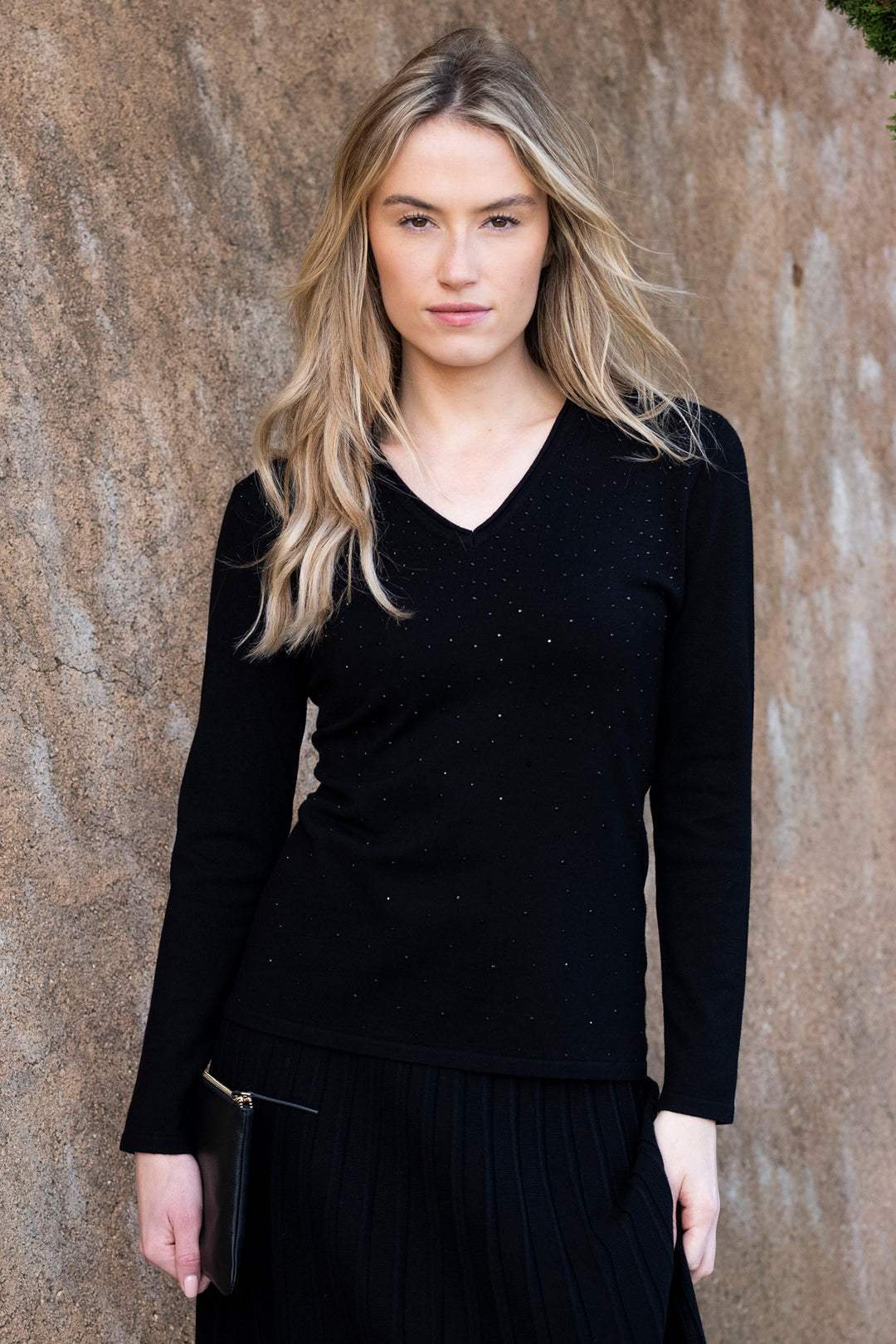 Woman wearing a black long-sleeve top against a textured wall.