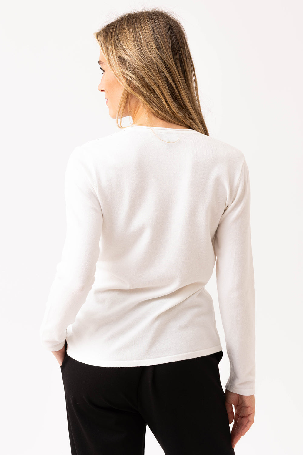 Woman wearing a white long-sleeve top and black pants on a white background