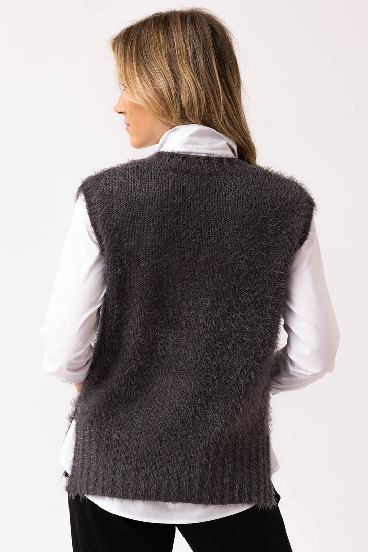 Person wearing a dark gray knitted vest over a white shirt on a plain background