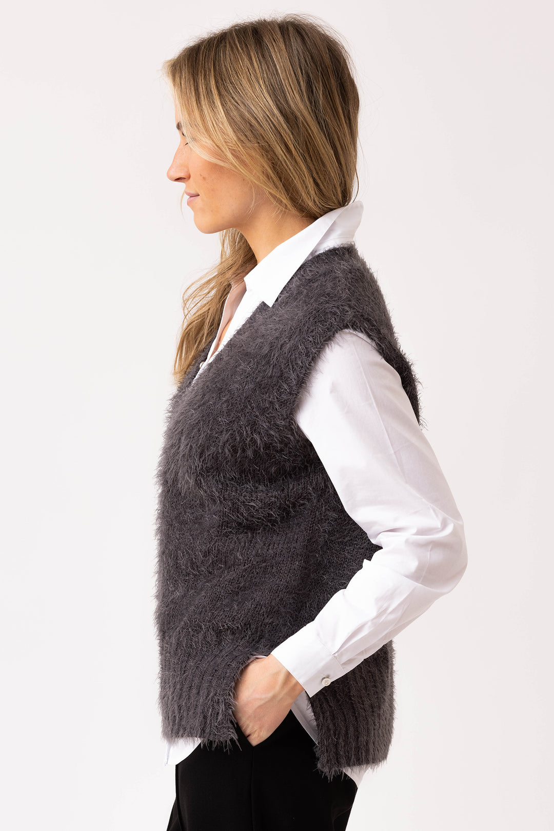 Woman wearing a dark gray knitted vest over a white shirt on a light gray background