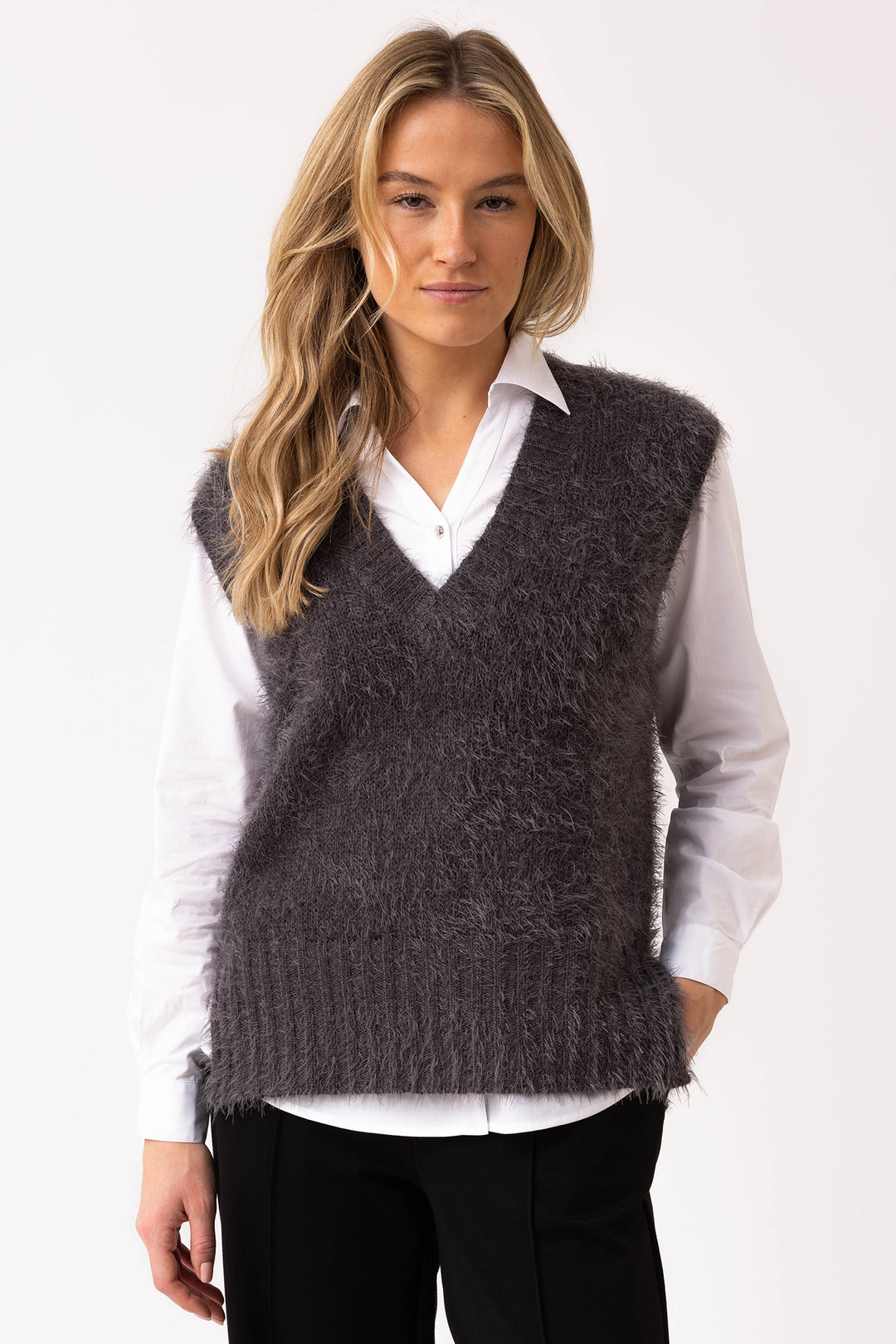 Woman wearing a dark gray knitted vest over a white shirt on a white background