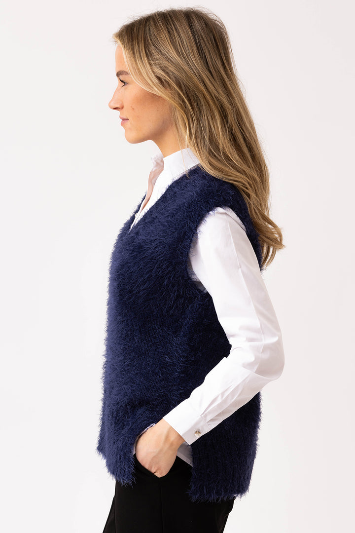 Woman wearing a navy blue fuzzy vest over a white shirt on a light gray background
