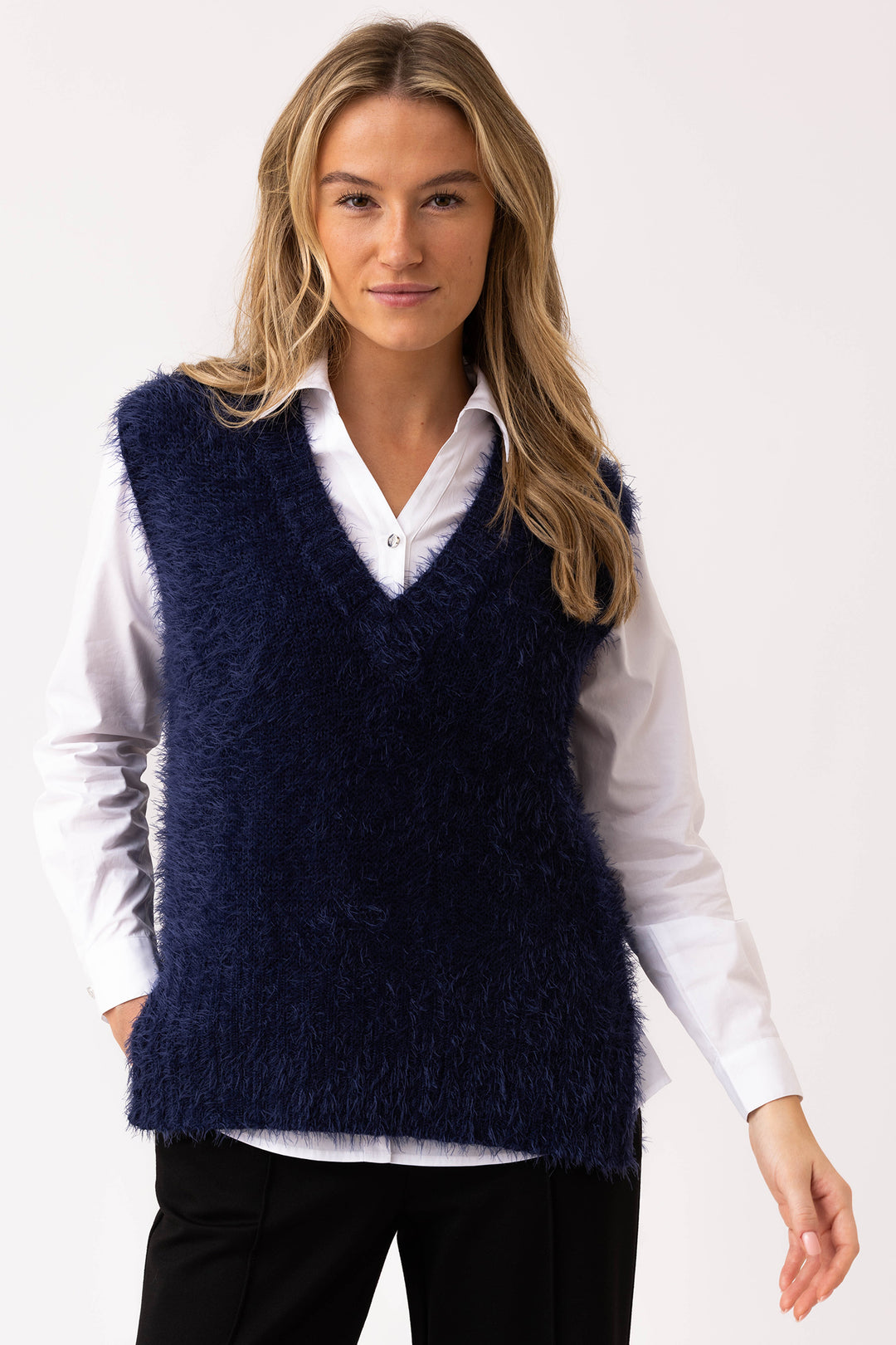 Woman wearing a navy blue fluffy vest over a white shirt on a white background