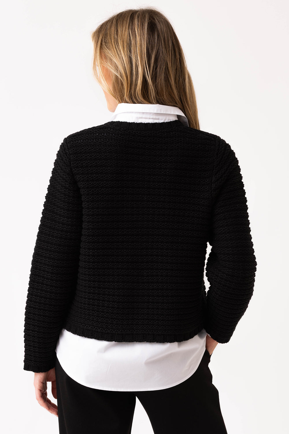 Person wearing a black textured sweater over a white shirt on a plain background