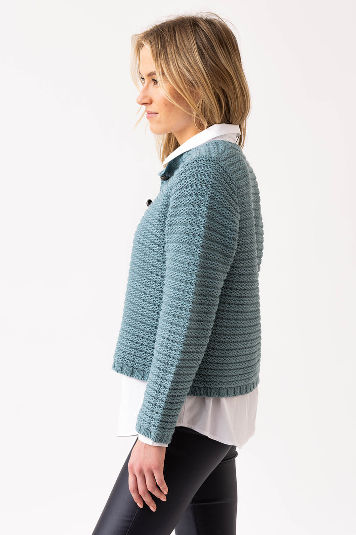 Woman wearing a textured blue sweater over a white shirt on a light gray background