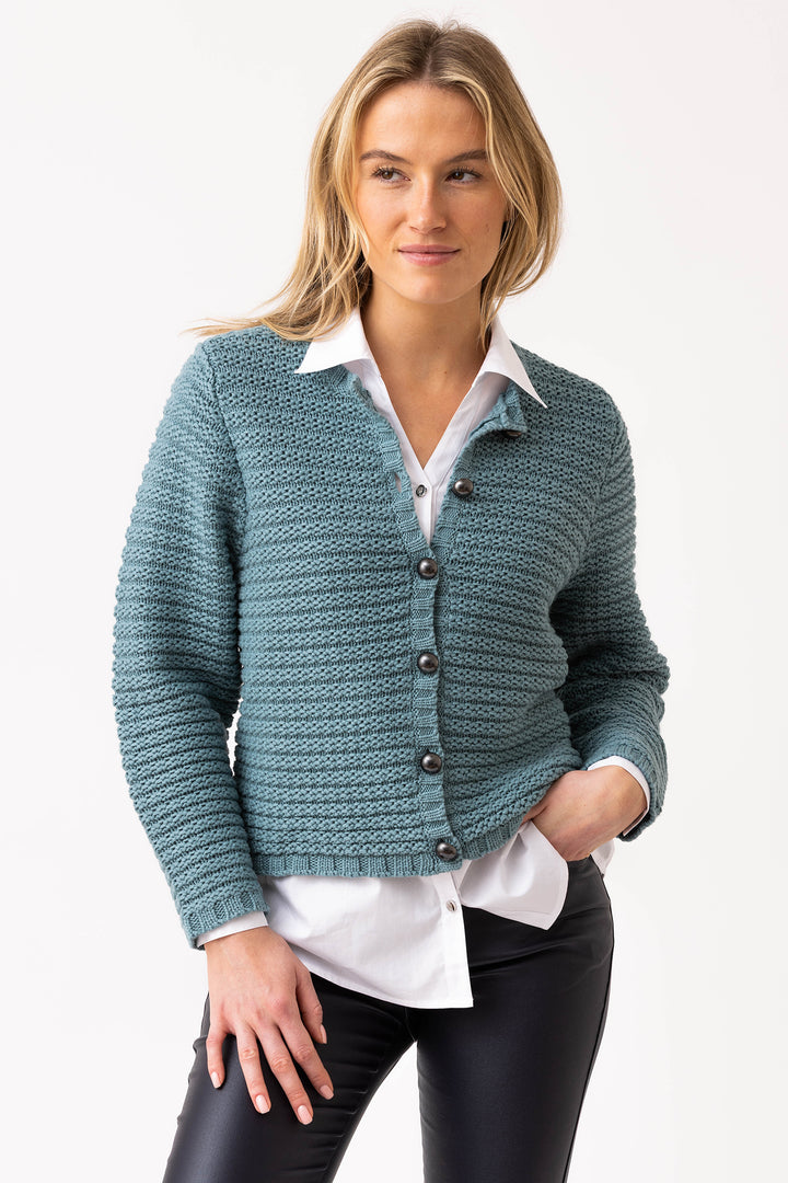 Woman wearing a teal knitted cardigan over a white shirt on a light gray background