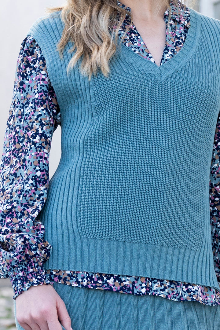 Teal knitted vest over a floral shirt with a blurred background