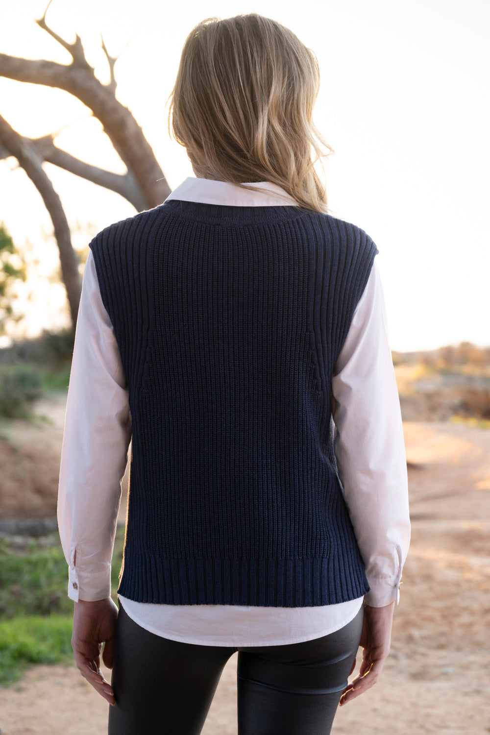 Person wearing a navy vest over a light shirt outdoors