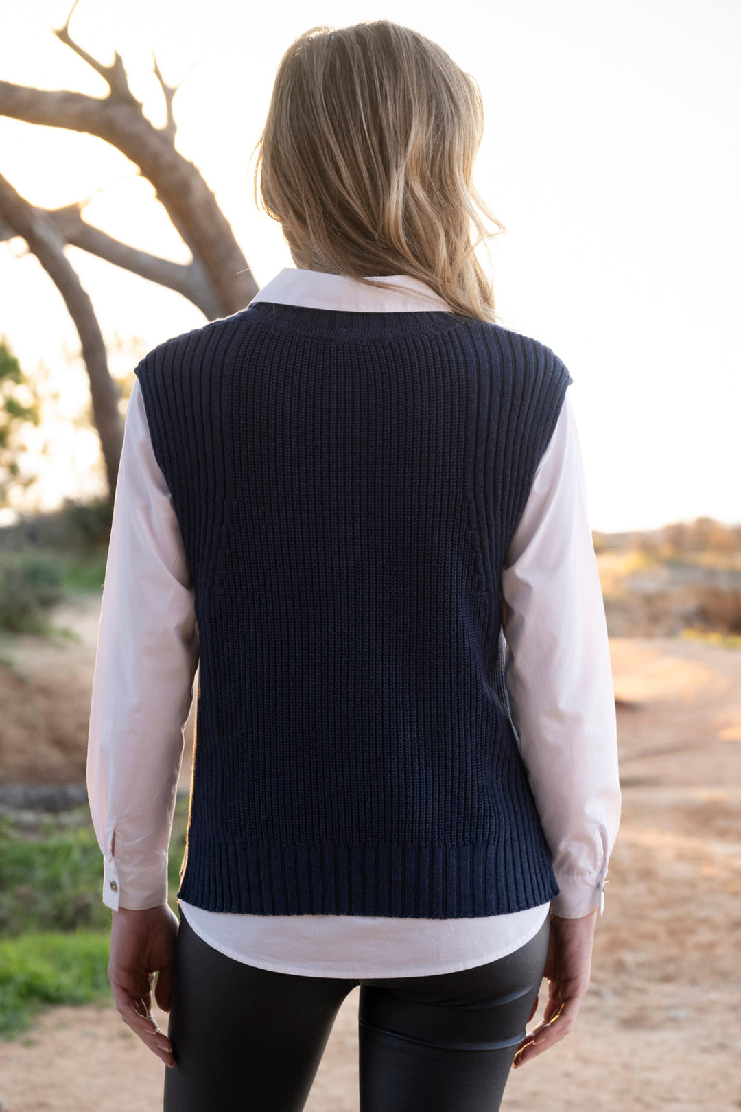 Person wearing a navy vest over a light shirt outdoors