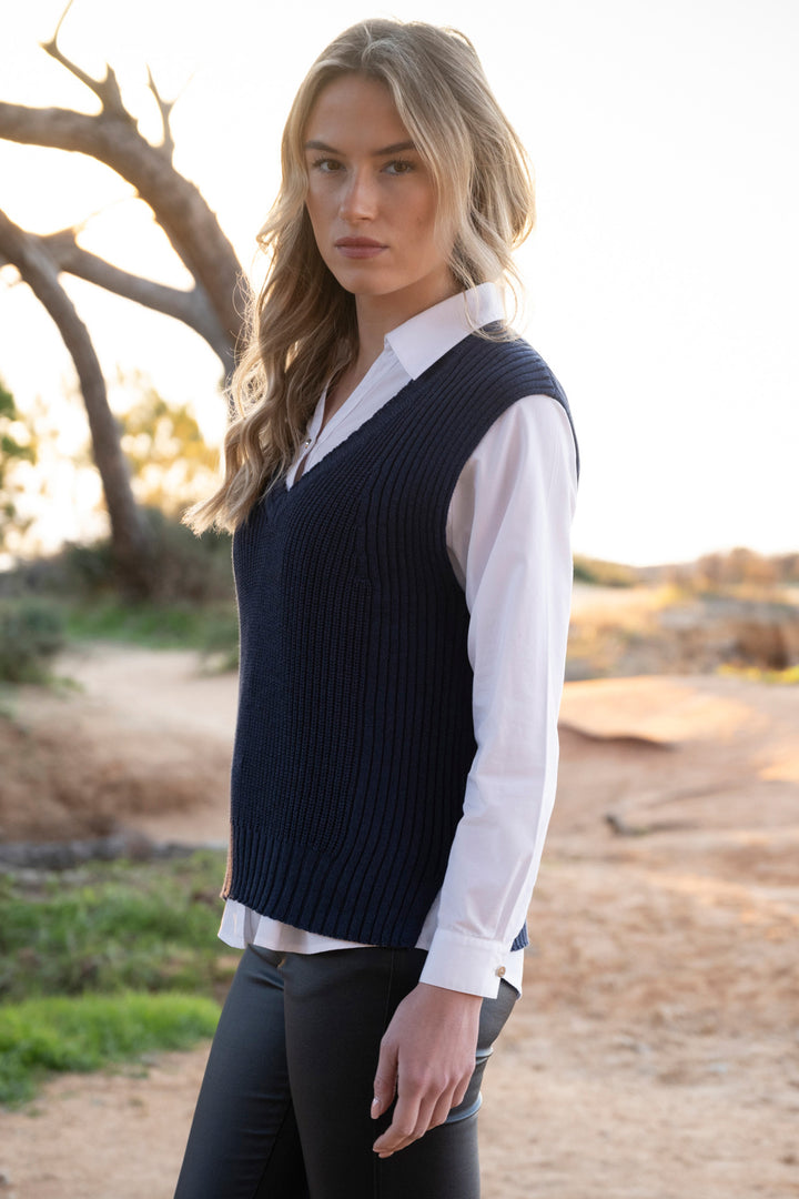 Woman wearing a navy sweater vest over a white shirt outdoors.