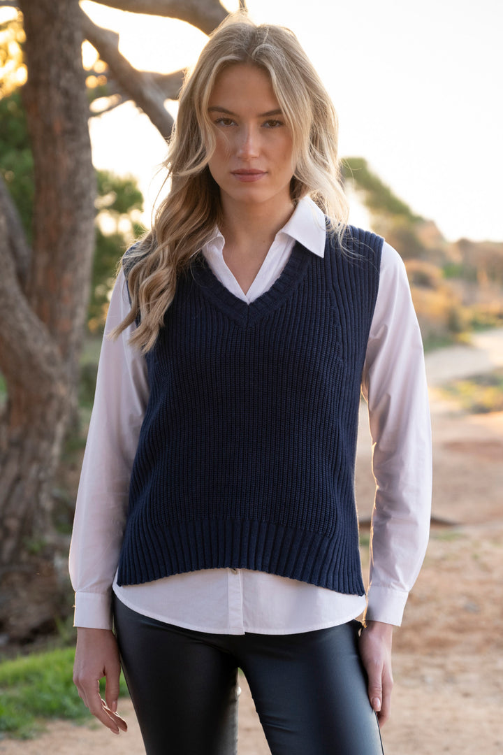 Woman wearing a navy sweater vest over a white shirt outdoors.
