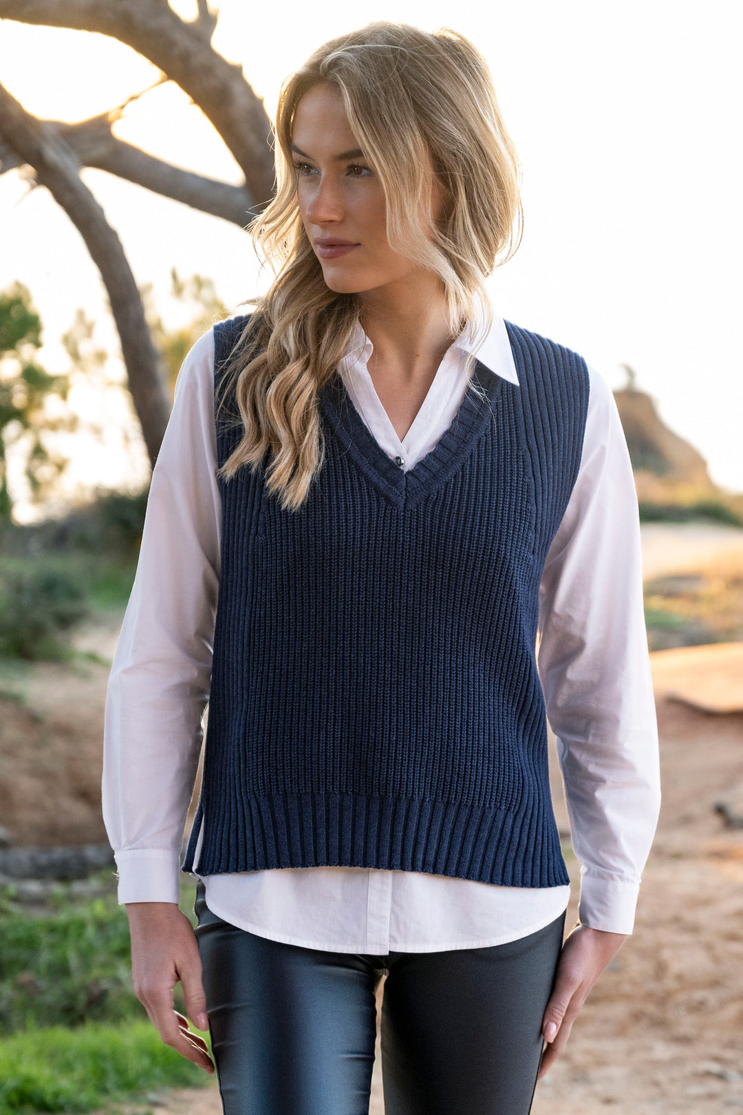 Woman wearing a navy sweater vest over a white shirt outdoors.