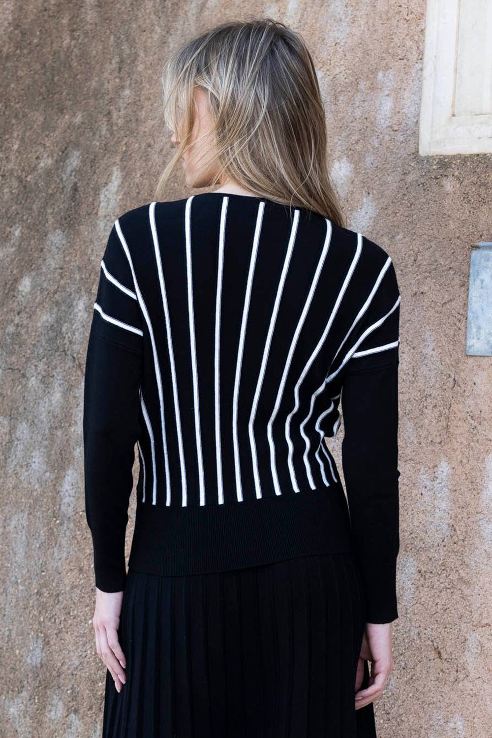 Person wearing a black and white striped sweater against a textured wall.